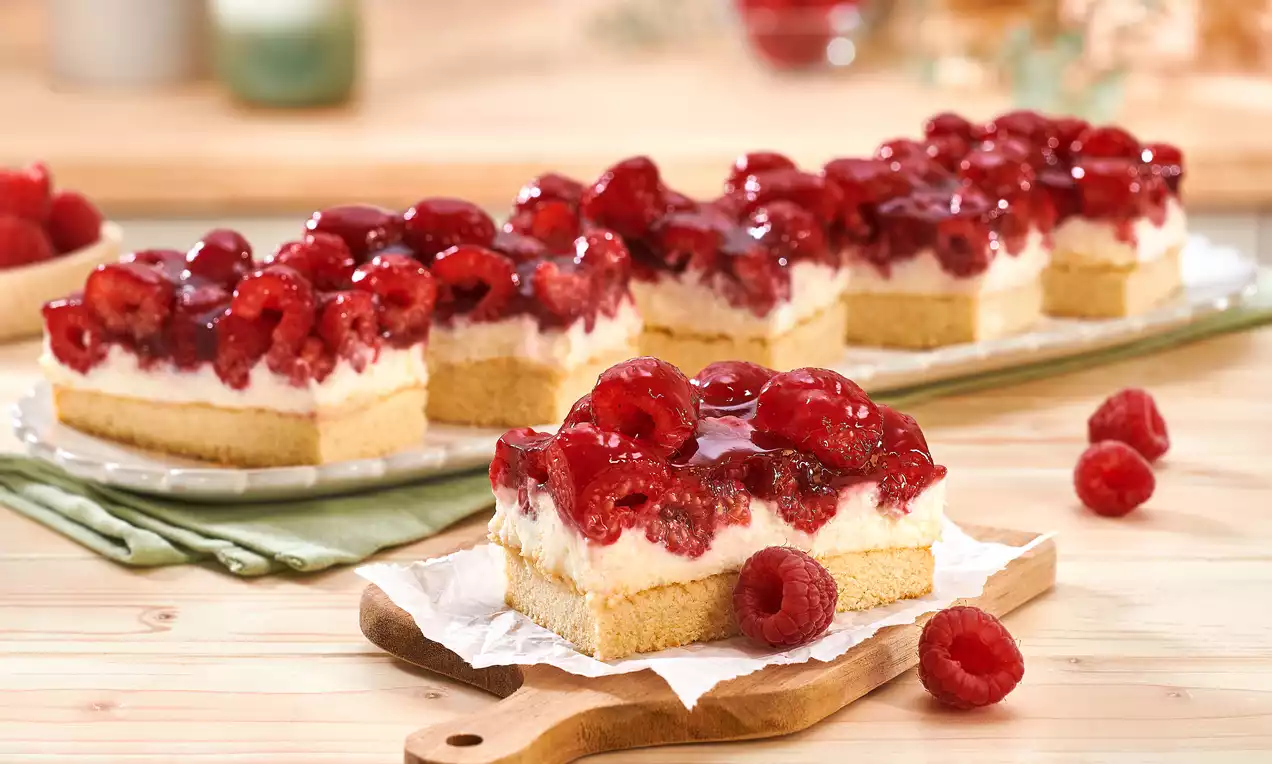 Himbeerrote Schnitten mit glasierten Beeren, cremeweißer Schicht und hellem Boden, serviert auf Holzbrett mit frischen Himbeeren dekoriert