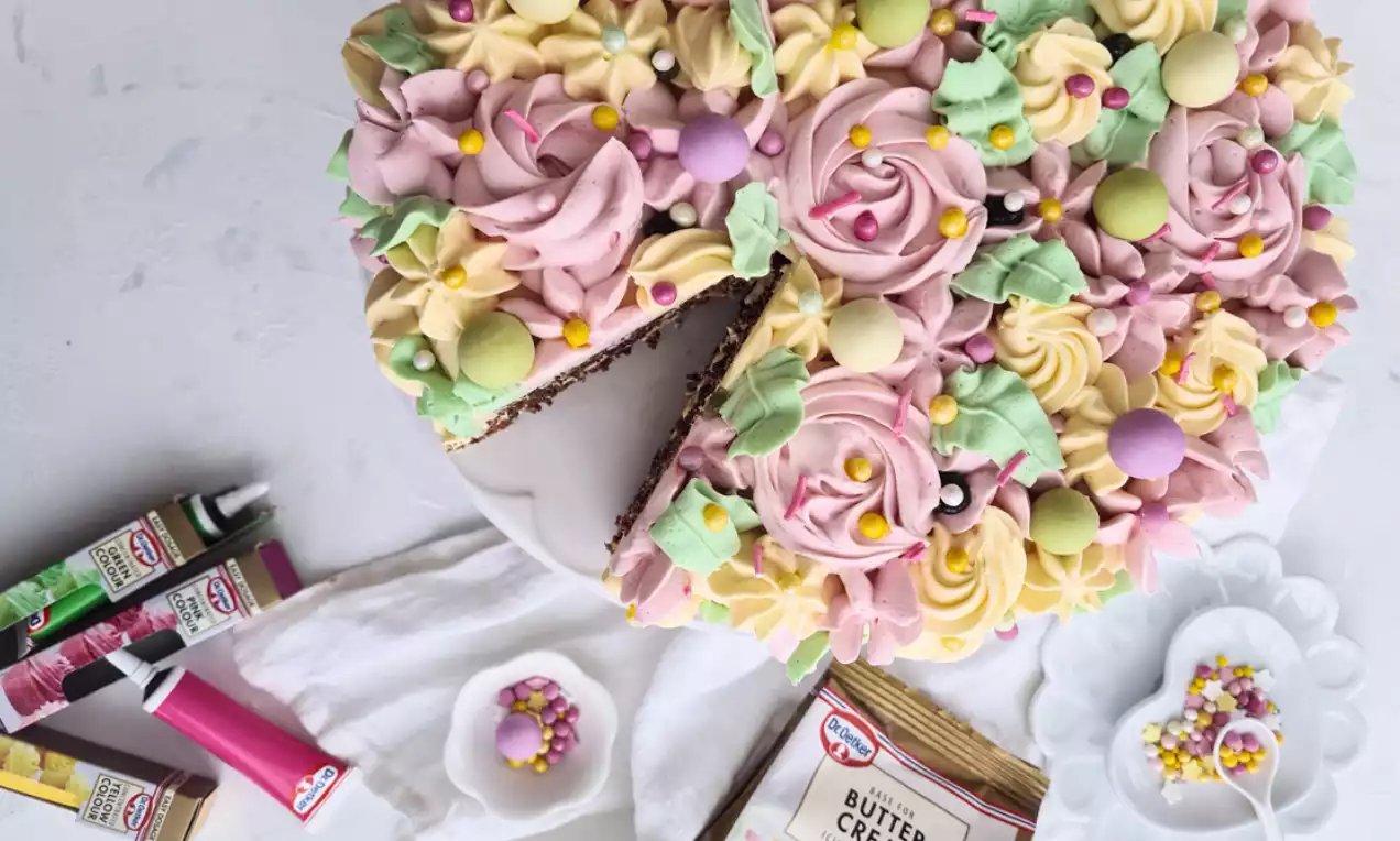 Choklad- och passionsfruktstårta med virvlande rosor av pastellfärgad smörkräm, gul och rosa, dekorerad med små strösselkulor och godisar