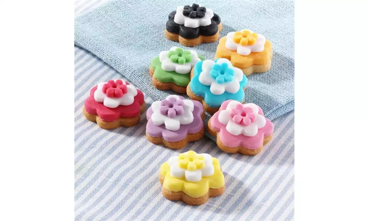 Petits sablés dorés en forme de fleurs avec un glaçage coloré pastel disposés sur un linge rayé bleu et blanc