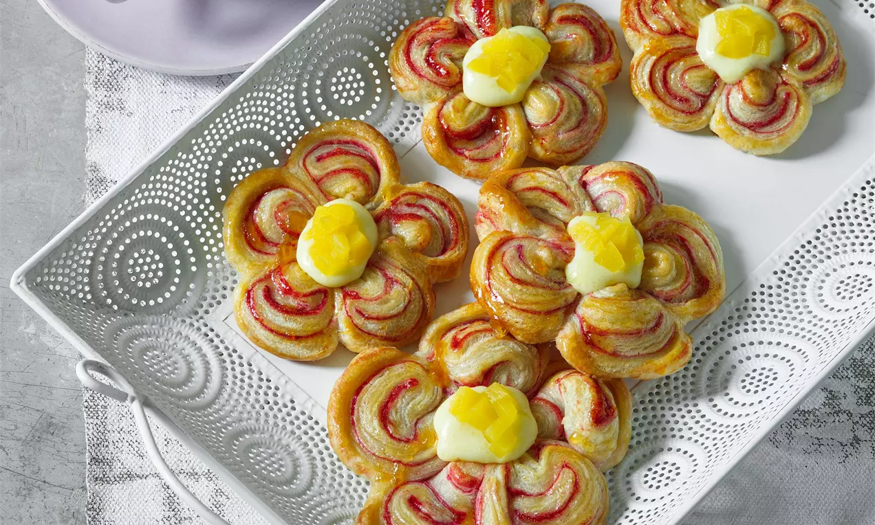 Lístkové kvety s marhuľovým a jahodovým vzorom, v strede žltý krém, na bielom vyrezávanom podnose s jemným krajkovým detailom