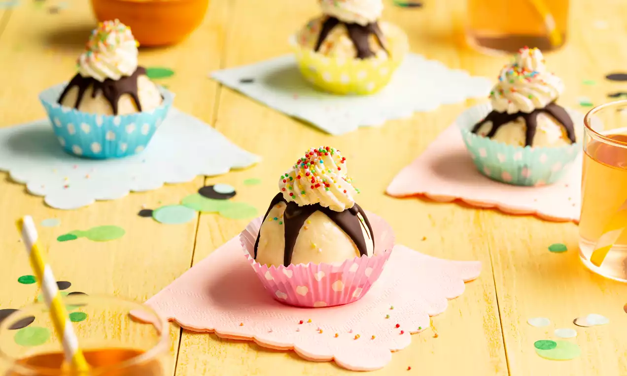 Cupcakes in pastelgekleurde papieren vormpjes, met vanilleijs, chocoladetopping, slagroom en kleurrijke sprinkles op een houten tafel