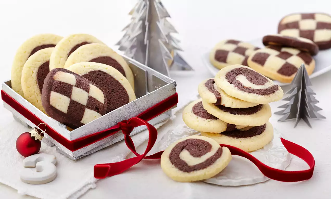 Schwarz-weißes Gebäck mit zarter Mürbeteig-Textur als Karomuster und Spiralen arrangiert in einer Schale und auf weißem Untergrund