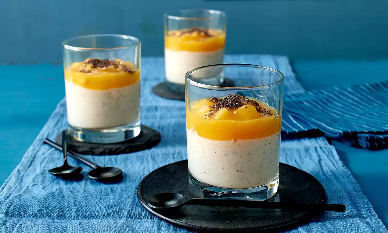 Gläser mit heller, gesprenkelter Mohn-Buttermilch-Creme, bedeckt von leuchtend orangefarbener Fruchtsoße und dunklen Mohnstückchen
