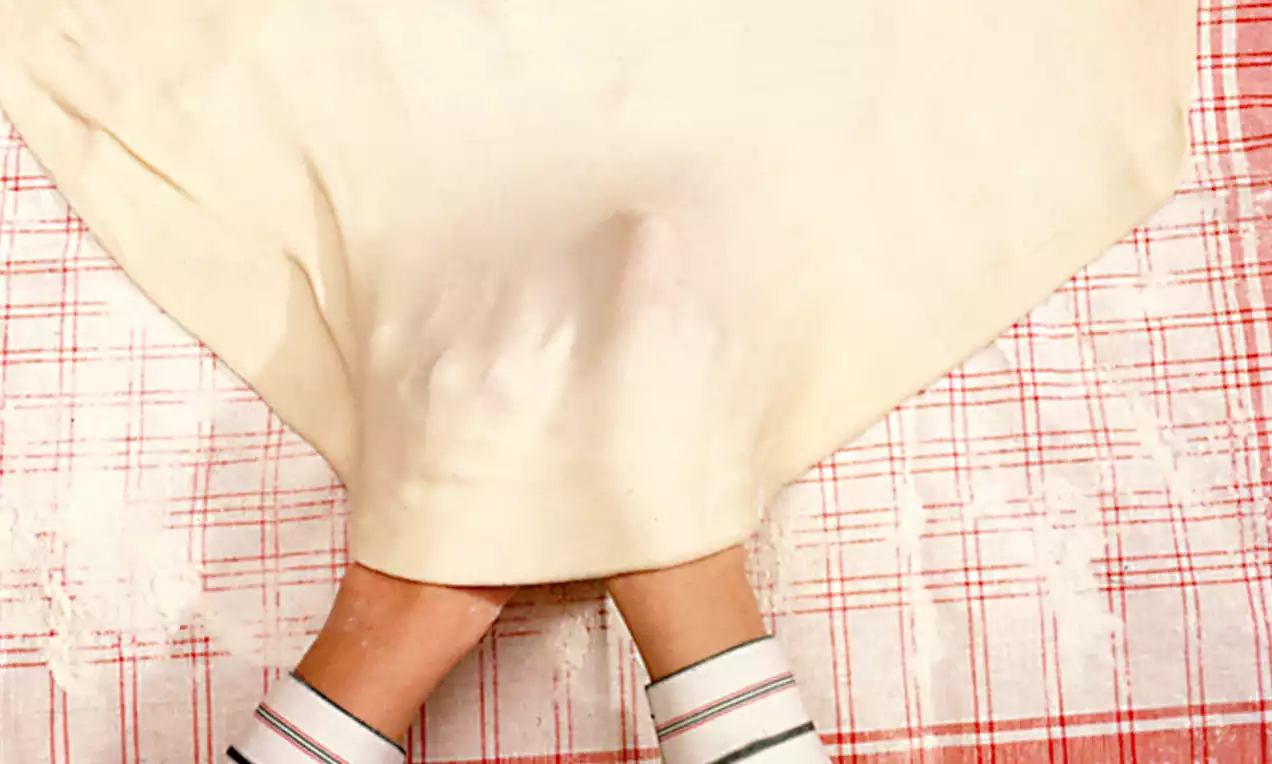 Strudelteig dünn und hell, sanft gezogen mit beiden Händen, auf rot-weiß kariertem Tuch mit leichtem Mehlstaub