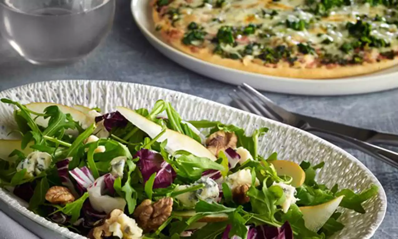 Salade colorée mélangée de roquette, radicchio, noix, poires jaune pâle et morceaux de gorgonzola crémeux dans une assiette texturée
