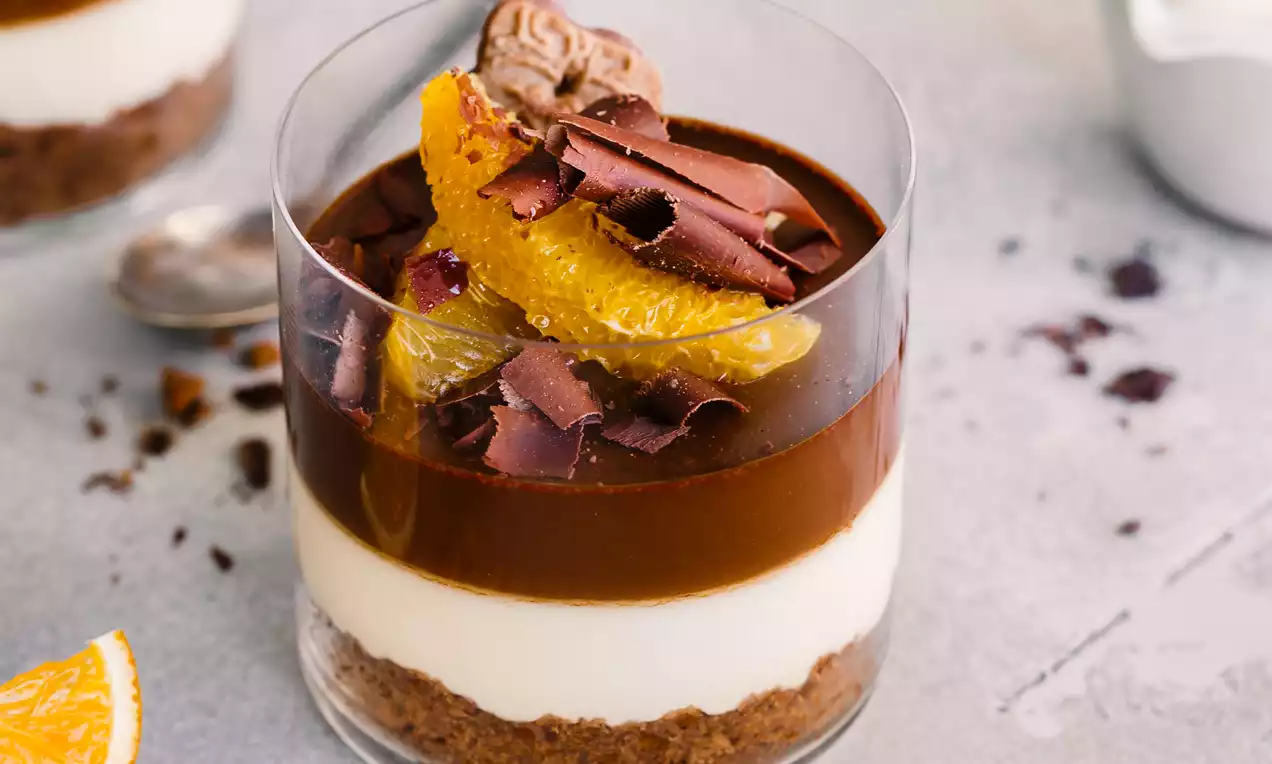 Picture - Vanilla Chocolate Pots de Creme layered in a glass with creamy white and rich brown, topped with orange slices and chocolate shavings
