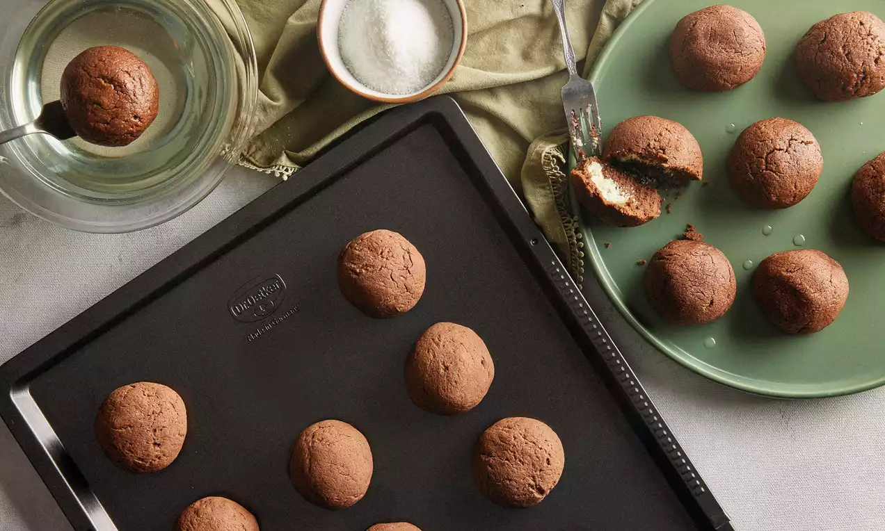 Kakaolu hamurun yuvarlak toplar halinde pişirildiği, içi beyaz hindistan cevizi dolgulu kurabiyeler yeşil bir tabakta ve tepsi üzerinde sergilenmiş 