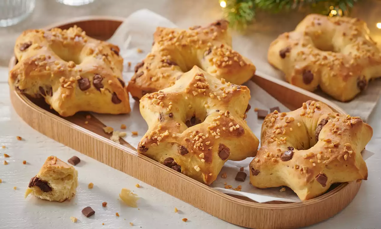 Goldbraune Hefesterne mit gerösteten Haselnüssen und Schokostückchen auf hellem Holztablett, dekoriert mit Tannenzweig und Lichtern