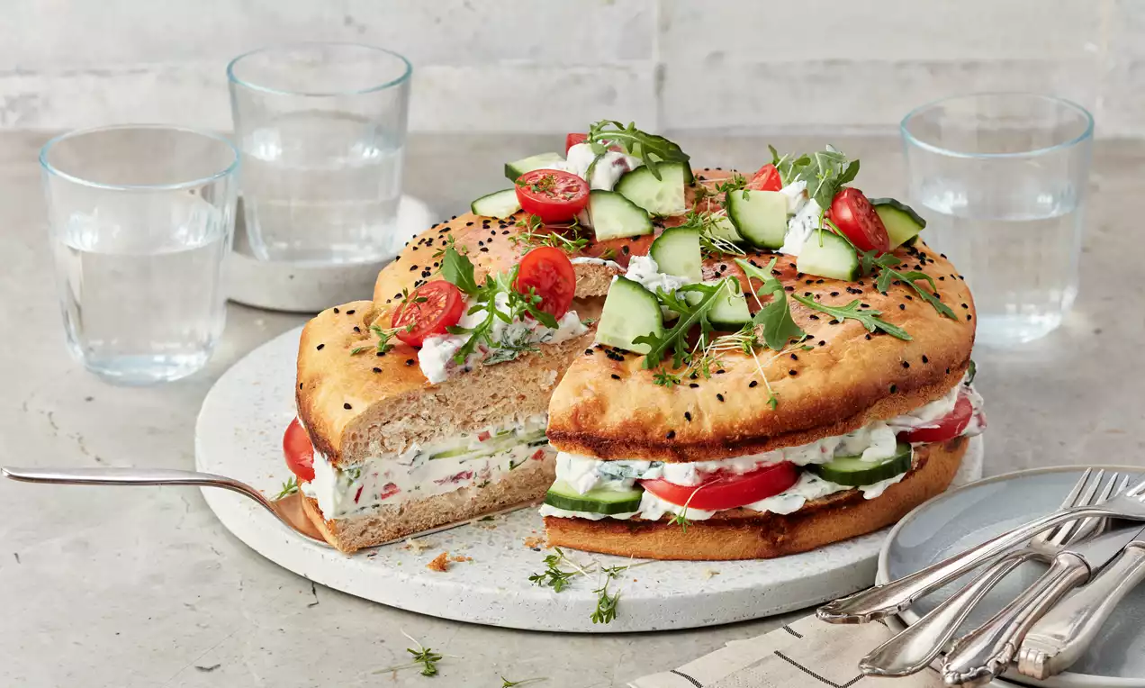 Herrentorte herzhaft mit cremiger Frischkäsefüllung, Schinkenstreifen, buntem Gemüse und Kräutern, auf rustikalem Servierteller