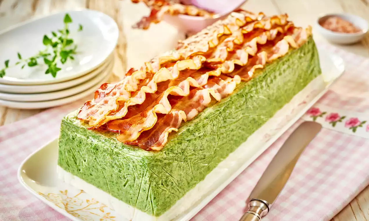 Prostokątna terrina warstwowa w kolorach bieli i zieleni, zwieńczona chrupiącymi plasterkami boczku na wzorzystym półmisku na kraciastej ściereczce