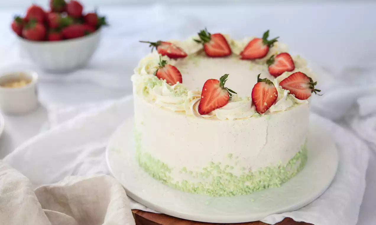 Lagkage med hvid flødeskumsbeklædning, grøn krymmel på siderne og pyntet med hele friske jordbær placeret på kantens top