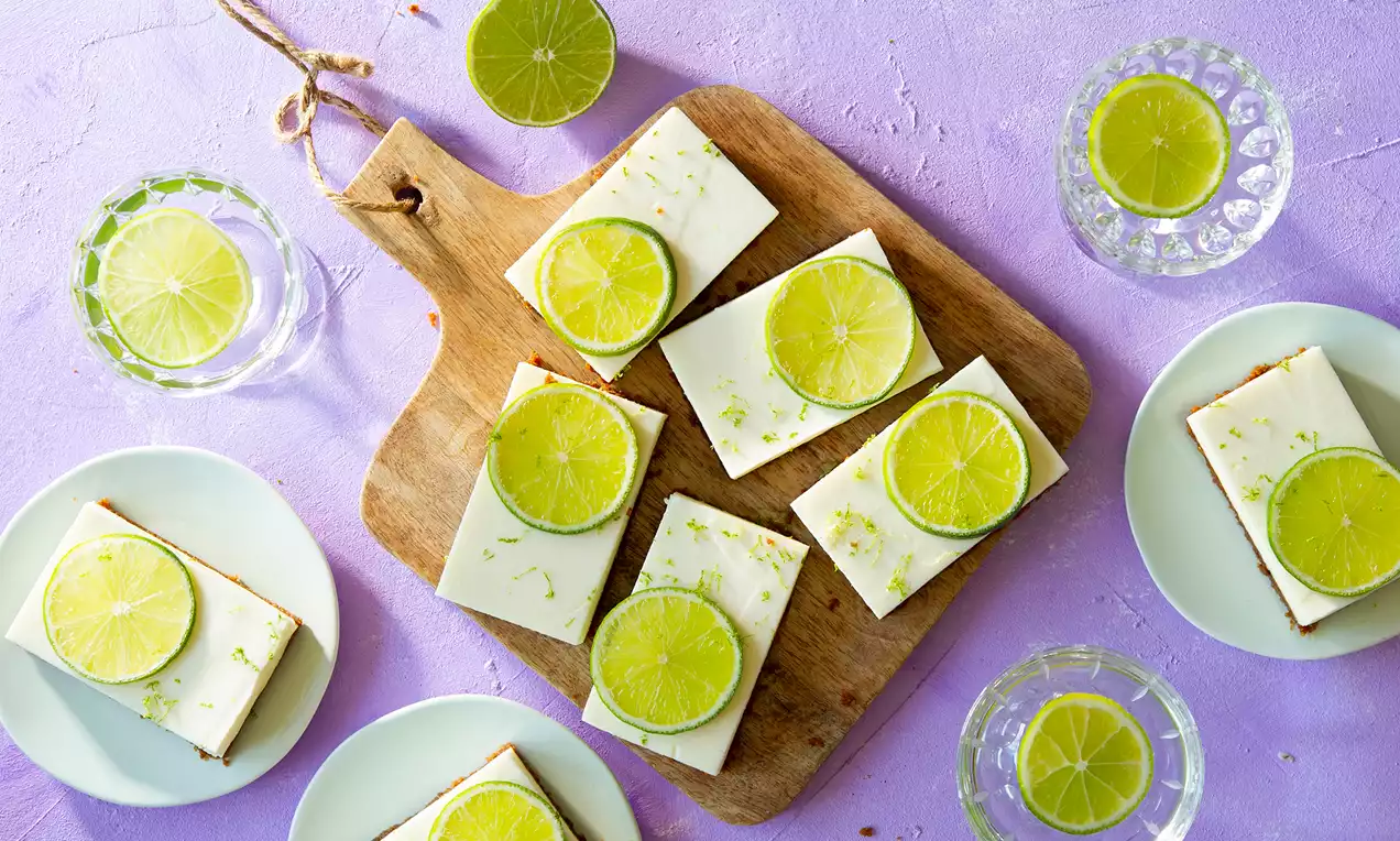 Rechthoekige limoentaartjes met romige, witte topping en heldergroene limoenplakjes, geserveerd op een houten plank en witte bordjes