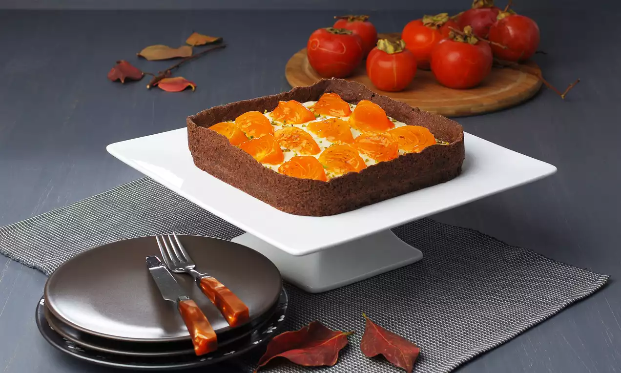 Kakaolu tabanlı kare tart, kremalı dolgusu üzerinde dilimlenmiş parlak turuncu cennet meyveleriyle bir pasta standında sunulmuş