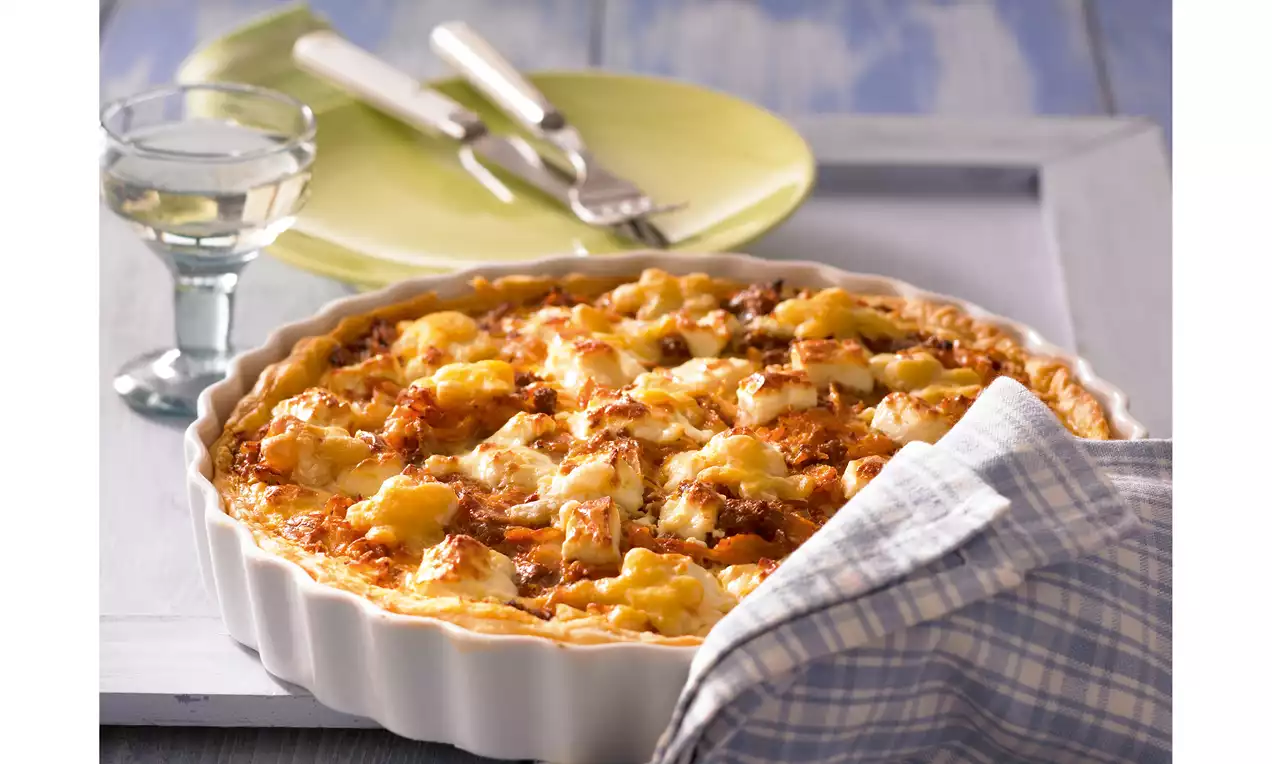 Goldbraune Weißkohl-Blätterteig-Quiche mit knusprigem Rand, saftiger Füllung und überbackenem Käse in weißer Tarteform mit Geschirrtuch drapiert