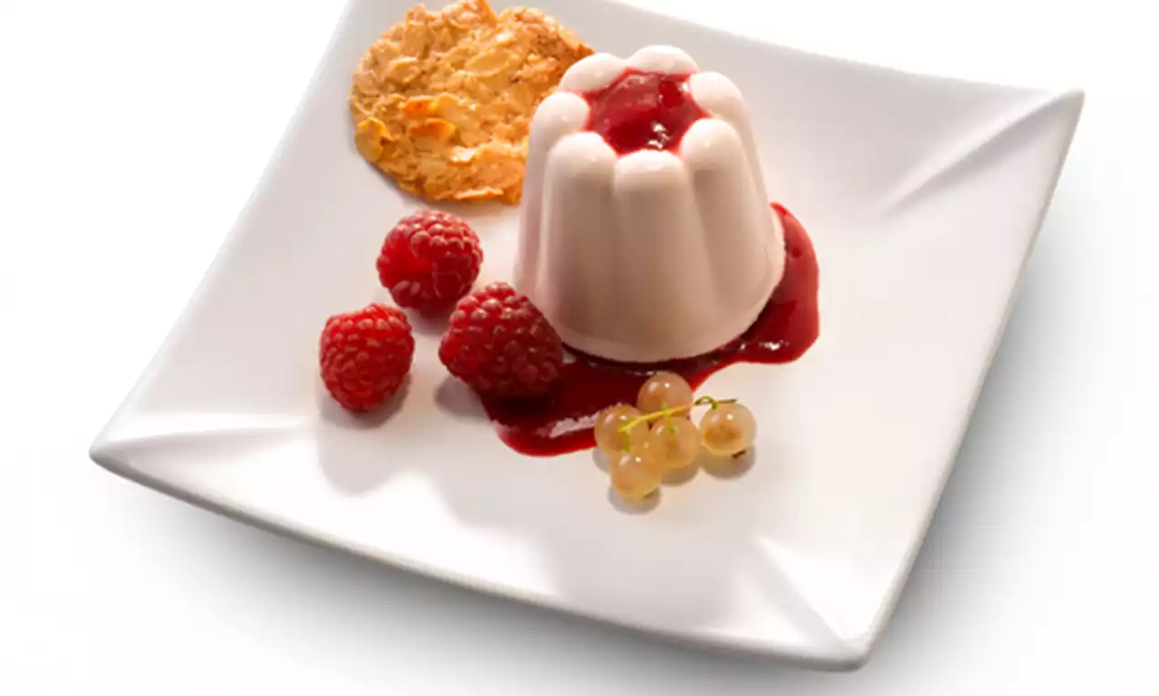 Lichtroze charlottepudding met ribbels, omringd door frambozensaus, verse frambozen, een knapperig koekje en gouden bessen op een wit bord