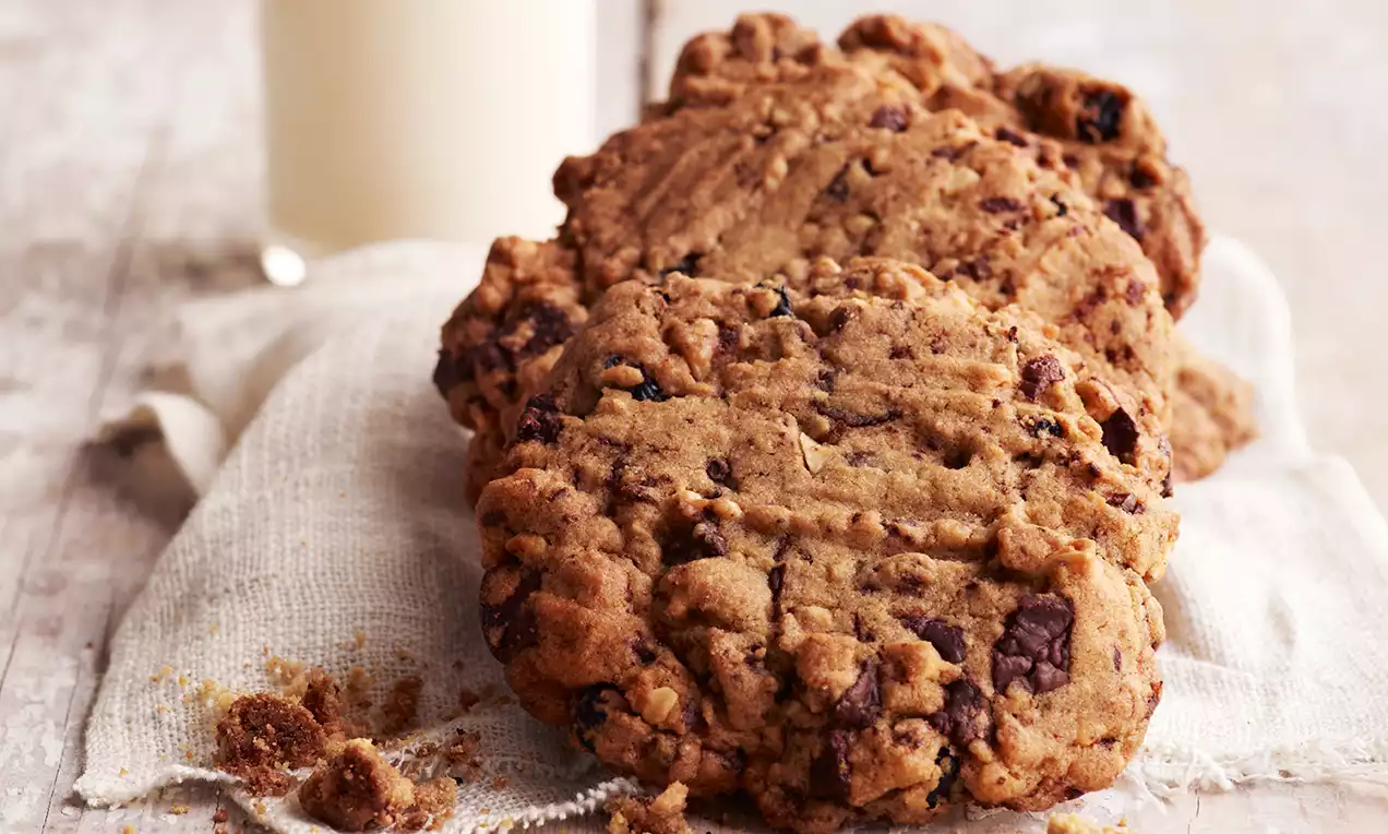 Amerikkalaiset cookiet pyöreän epäsäännöllisiä, rosoisen rapeita ja täynnä suklaanpaloja, aseteltuna pellavakankaan päälle vaalealla pöydällä