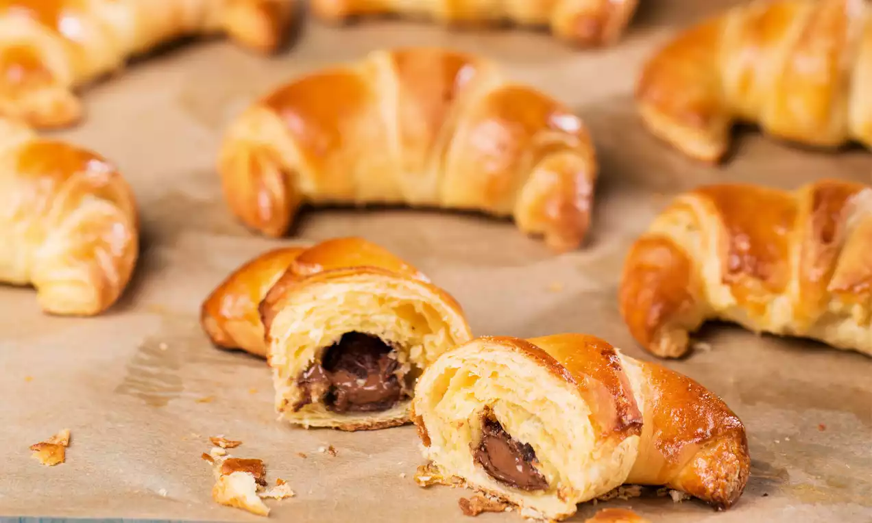 Zlatavé, lesklé croissanty s jemně vrstveným těstem, některé rozkrojené a odhalující čokoládovou náplň, na pečicím papíře