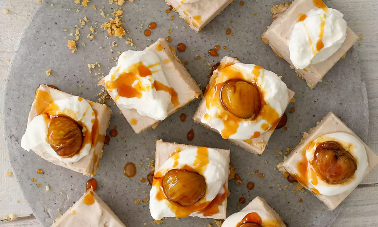 Carrés de pâte beige crémeuse surmontés de chantilly blanche, marrons caramélisés dorés et filet de caramel sur un plateau gris