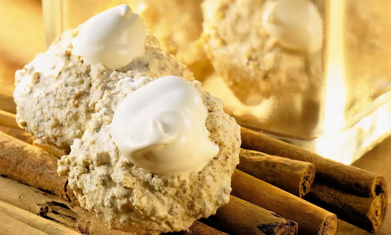 Petites meringues croquantes et beige doré surmontées de crème blanche, posées sur des bâtons de cannelle brun clair