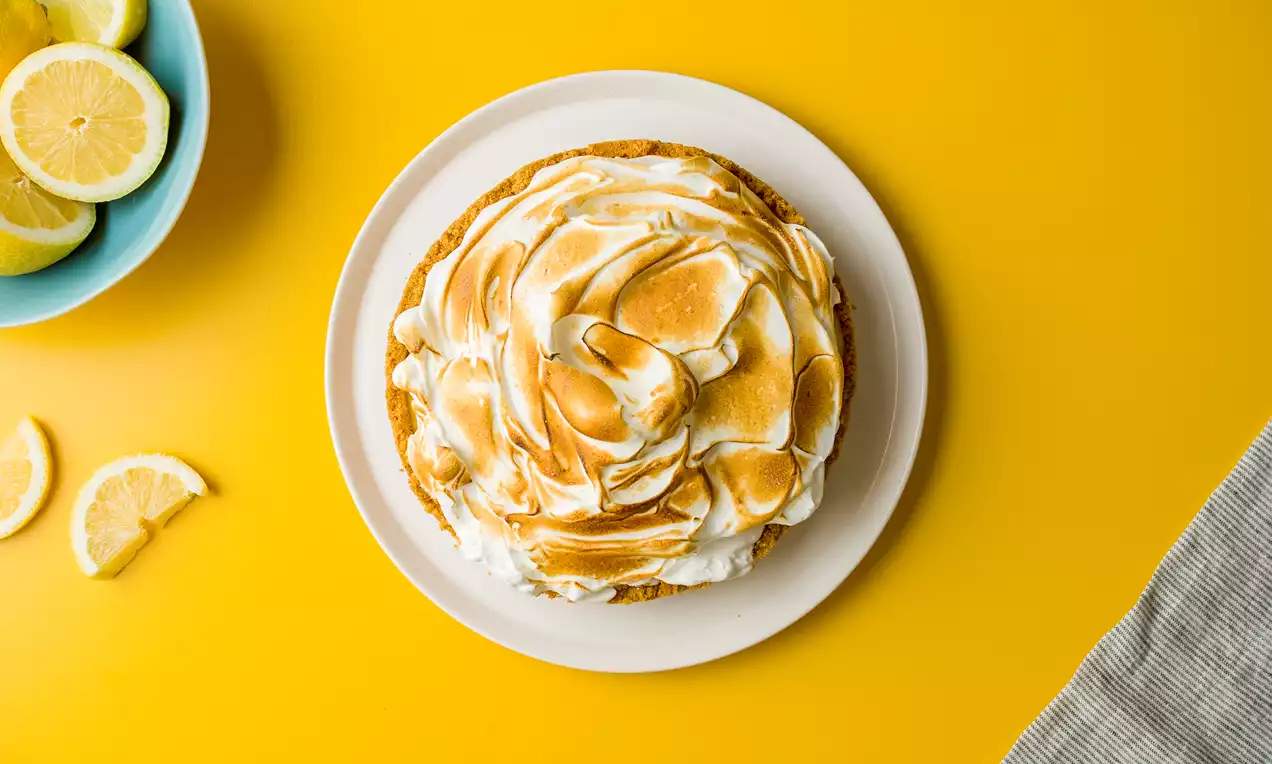 Lemon pie con cubierta de merengue dorado y textura ondulada sobre base dorada, en un plato blanco sobre fondo amarillo