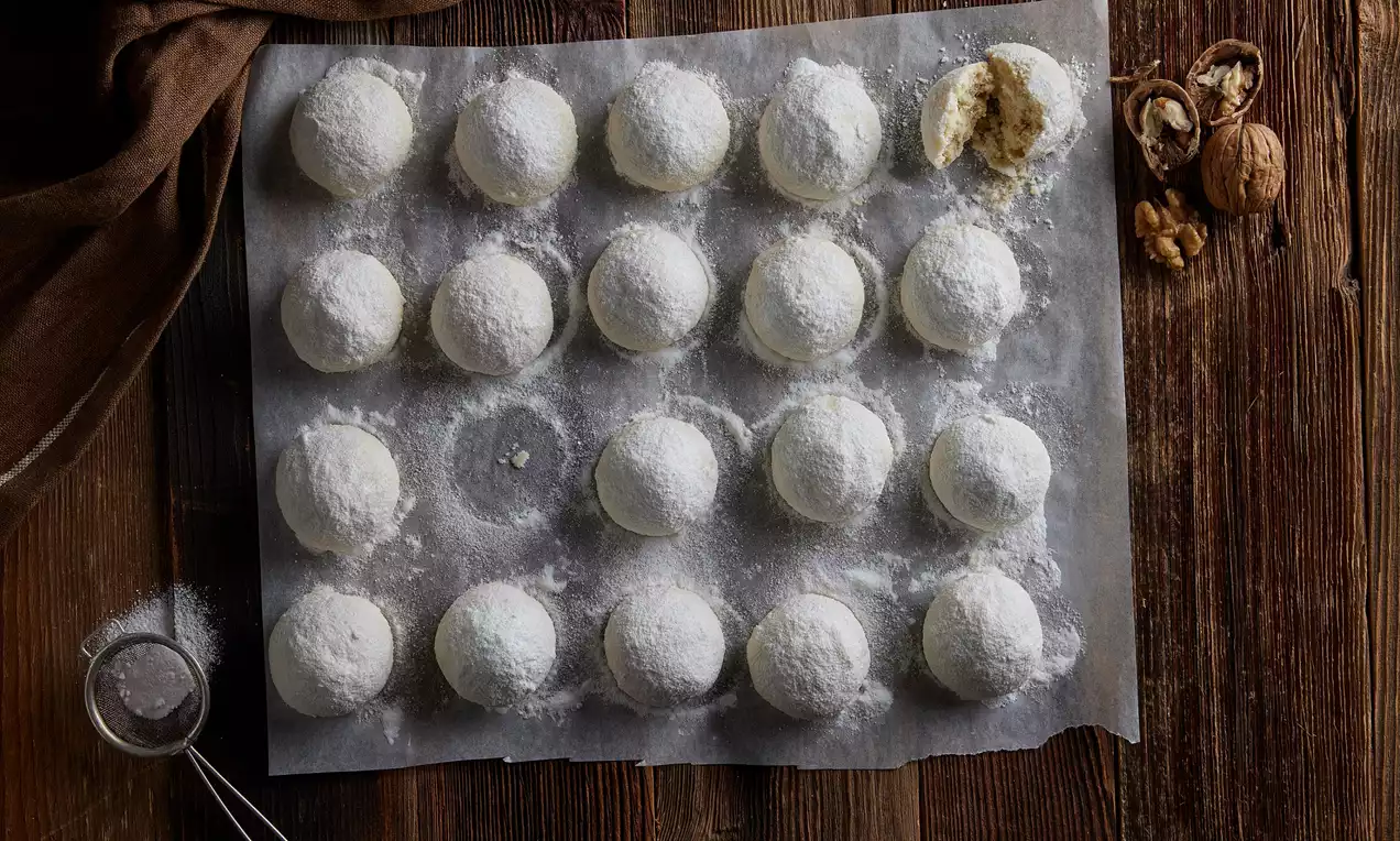 Meksika kurabiyeleri yuvarlak şekilli, beyaz pudra şekeriyle kaplanmış, kahverengi ahşap masa üzerinde yağlı kağıtta düzenlenmiş