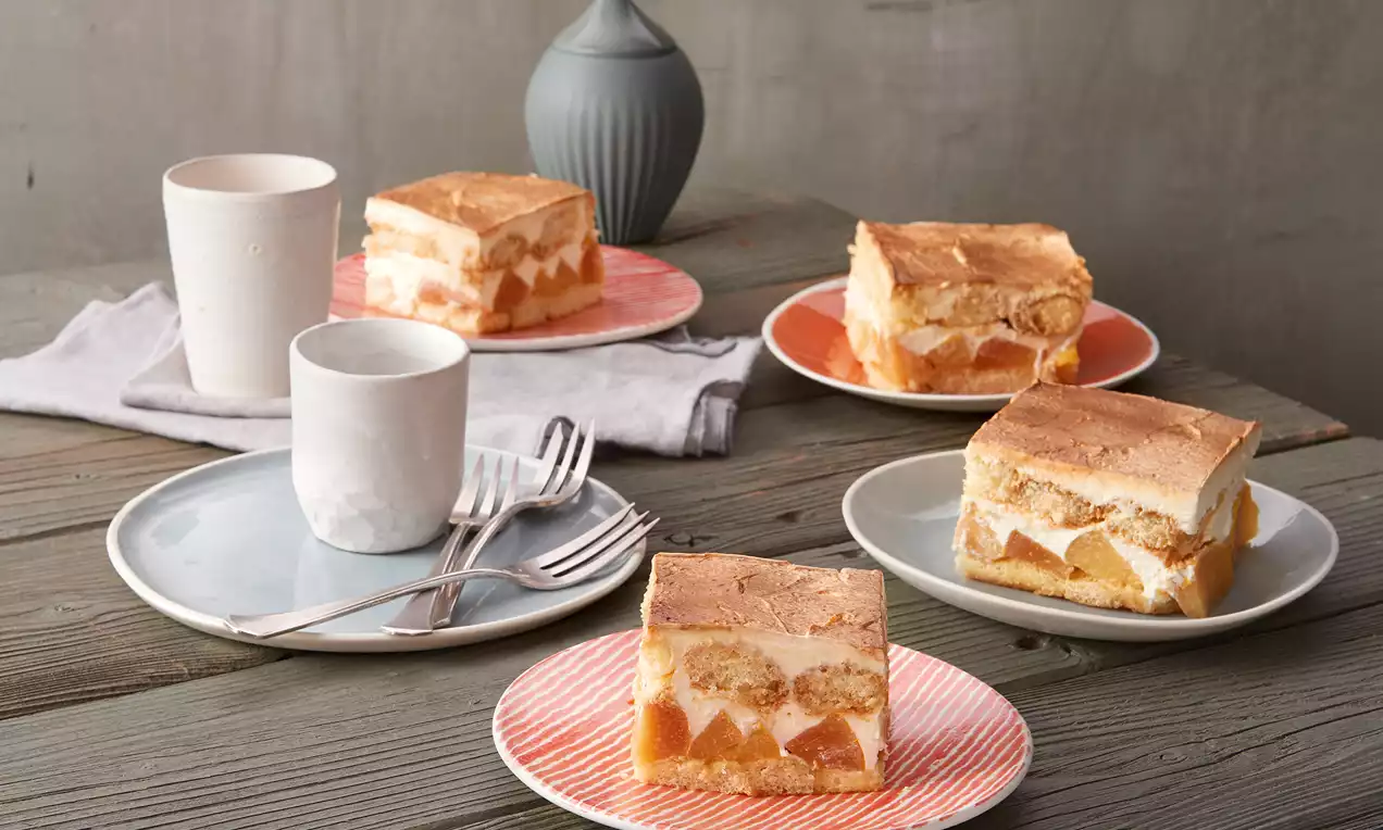 Quitten-Tiramisu mit goldbrauner Schicht und weicher Creme, durchzogen von Fruchtstücken, auf pastellfarbenen Tellern arrangiert mit Besteck
