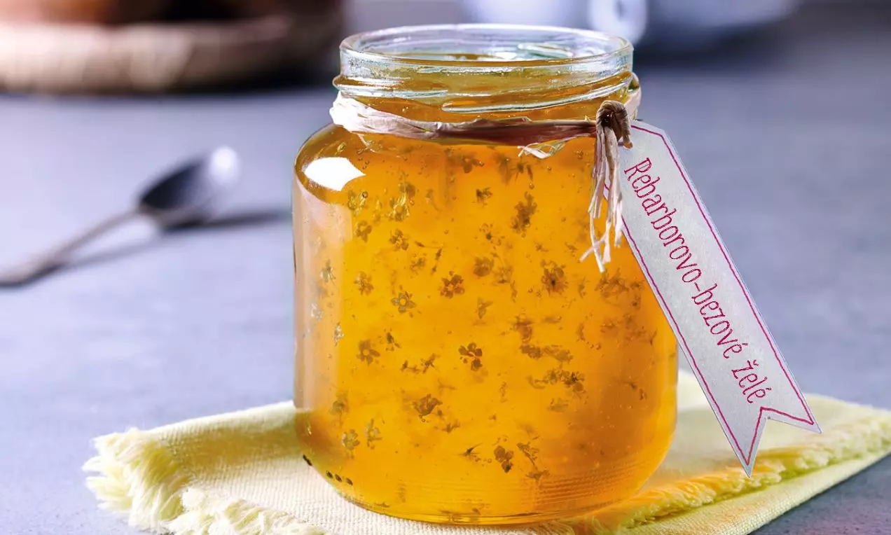 Sklenice plná průzračně zlatavého želé s drobnými kvítky uvnitř, ovázaná přírodním provázkem s papírovým štítkem na žlutém ubrousku