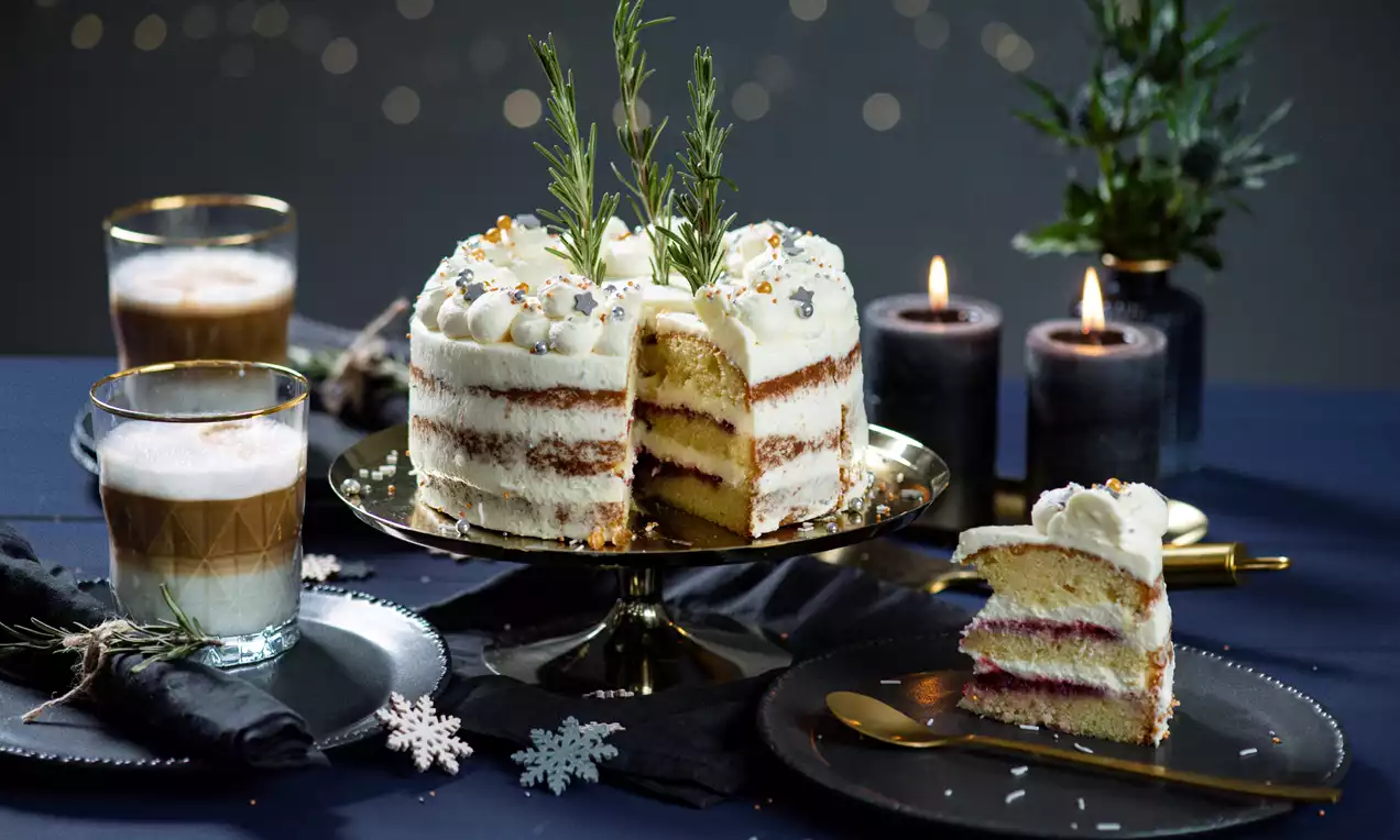 Christmas Naked Cake mit hellen Schichten und roter Füllung, dekoriert mit Sahnetupfen, Rosmarin und Zuckerstreuseln auf goldenem Teller