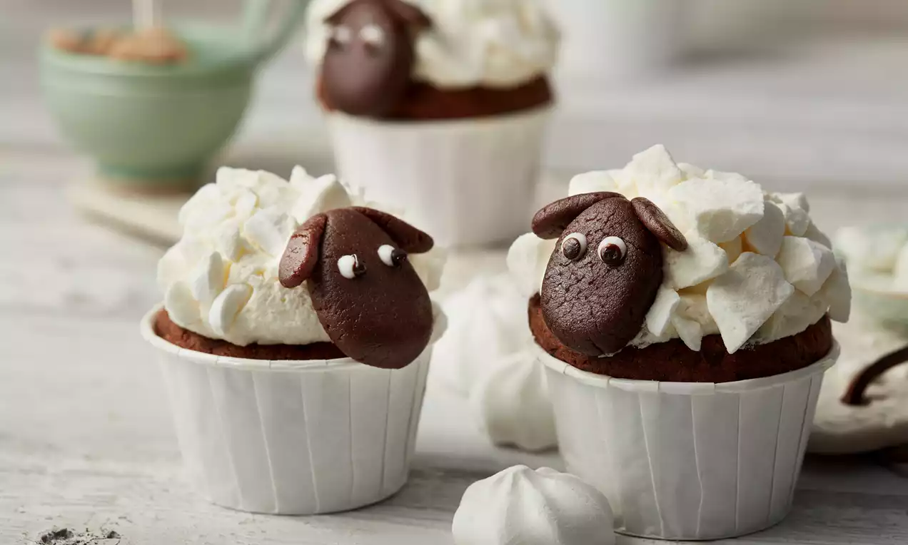 Kakao tabanlı cupcakeler, beyaz beze dokulu krema ile kaplı, çikolata parçalarından yapılmış kuzular ile süslenmiş kağıt kalıplarda