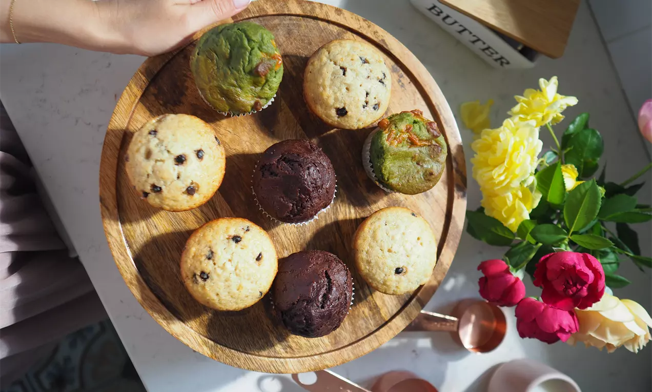 Пухкави мъфини в различни цветове, от тъмнокафяво до светлозелено, с хрупкава текстура, подредени в кръг върху дървена подложка