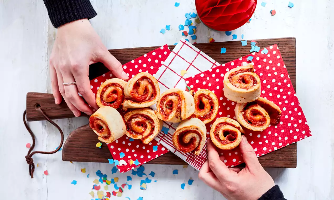 Pizza spiralată cu aluat rumen și umplutură de sos roșu dispusă pe șervețele roșii cu buline albe, pe un fund de lemn maro