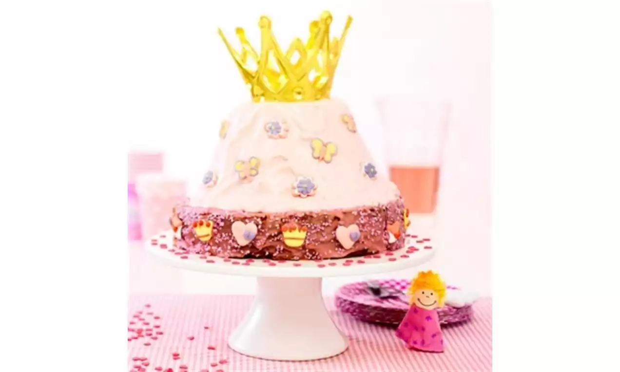 Hoge ronde prinsessentaart met roze en witte glazuurlagen, versierd met bloemen en hartjes, bekroond met een gele kroon, op een wit taartplateau