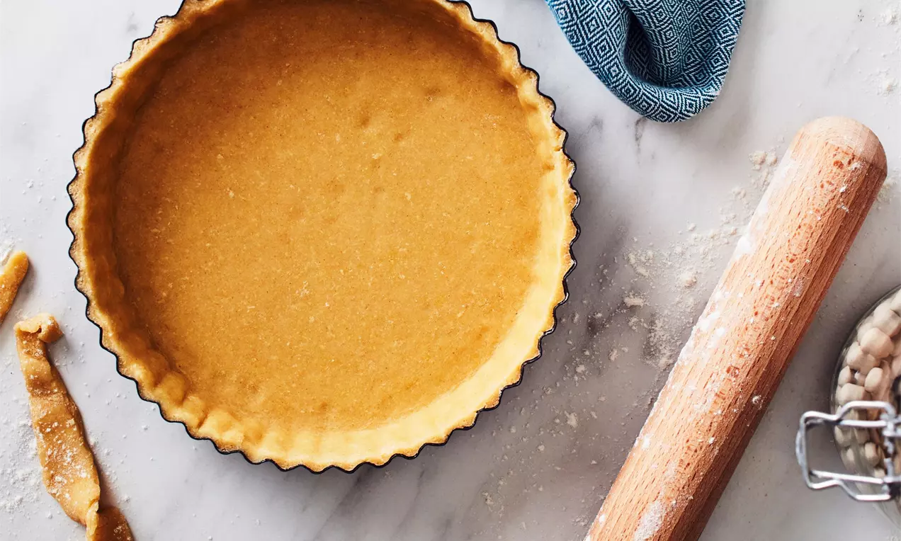 Светлозлатисто тесто с ронлива текстура, равномерно разположено във вълниста черна форма на мраморен фон с точилка и син плат