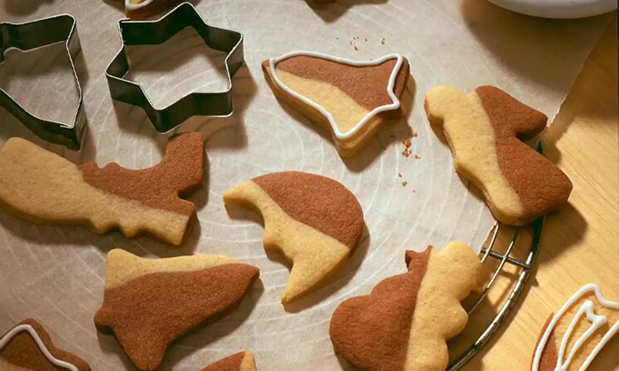 Schwarz-weiße Butterkekse in verschiedenen weihnachtlichen Formen, teils mit weißer Zuckerglasur verziert, auf Backpapier und einem Gitter verteilt