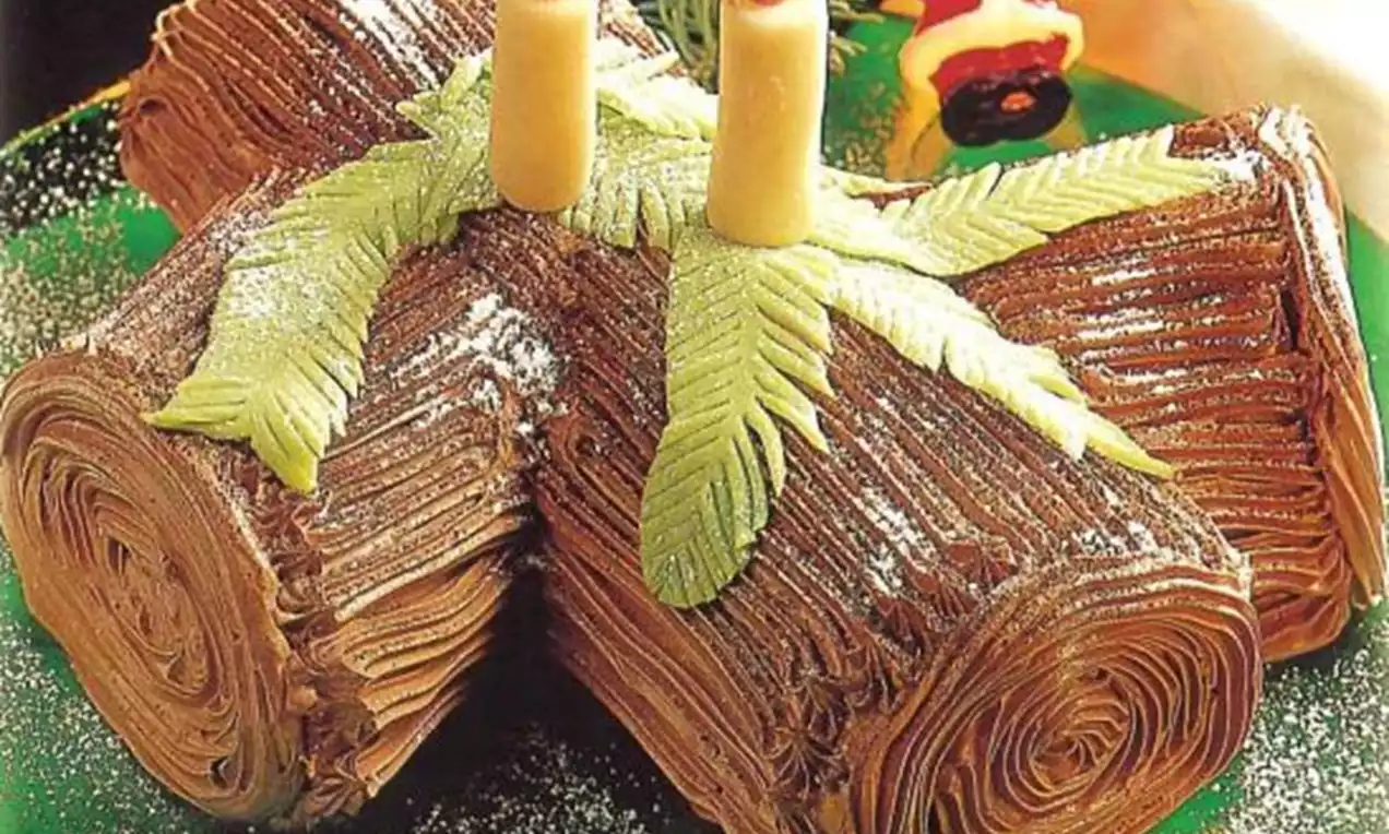 Bûche de Noël en chocolat texturée comme du bois, ornée de feuilles vertes en pâte d’amande et de bougies décoratives sur un plat vert