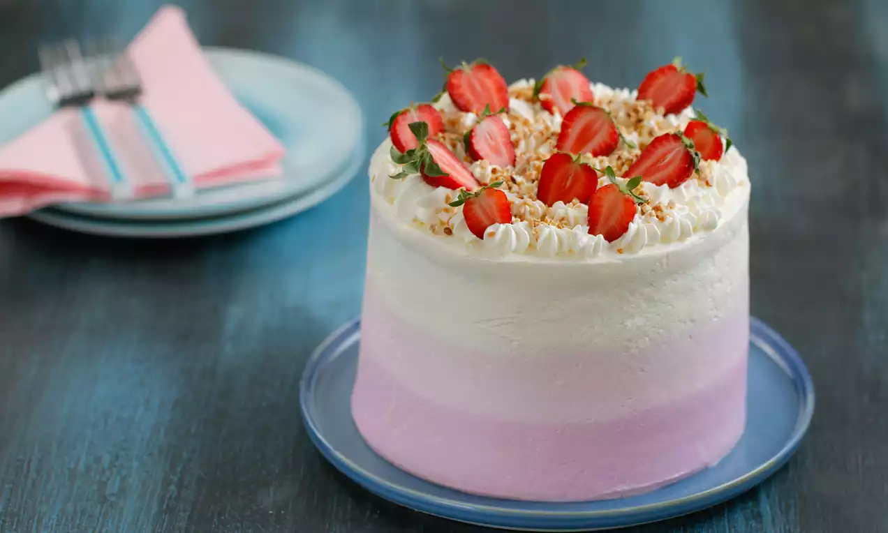 Yumuşak pembe ve beyaz tonlarda katmanlı, kremalı dolgun pasta, üstü taze çilek ve kıyılmış bademle süslenmiş mavi tabakta