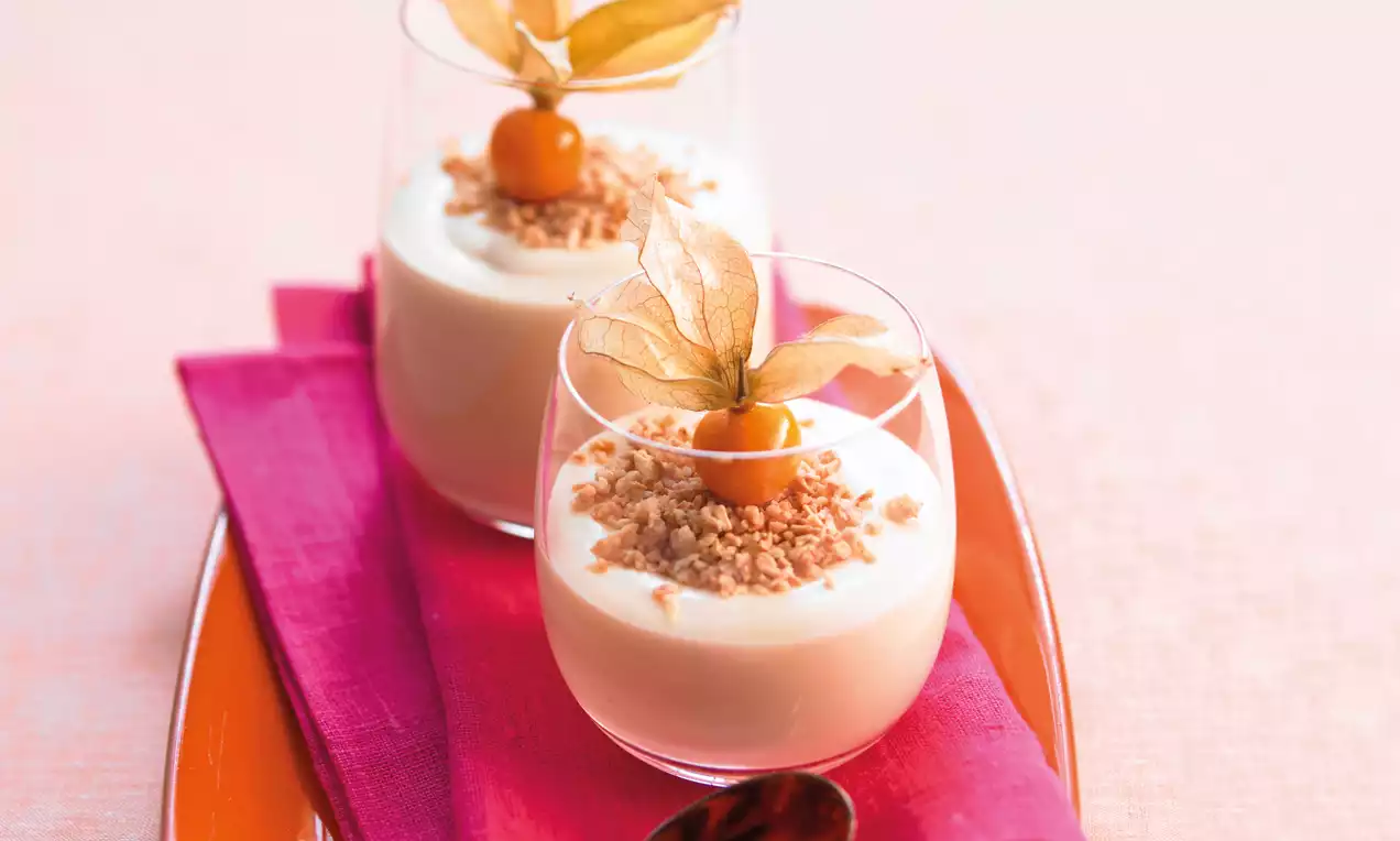 Crèmes onctueuses ivoire dans des verrines, parsemées de croustillant doré, surmontées de physalis et posées sur un plateau orange
