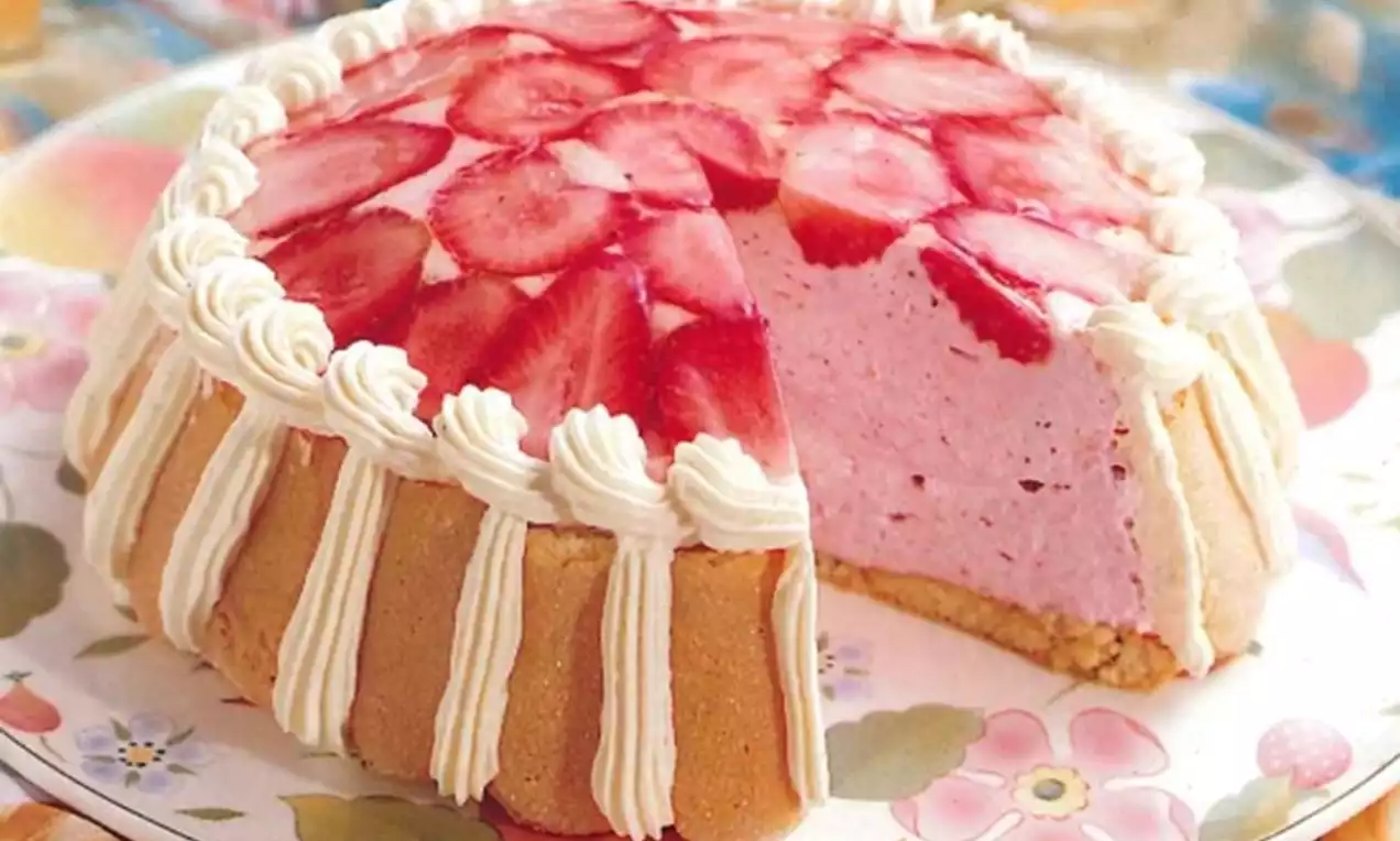 Aardbeiencharlotte met roze mousse, omringd door biscuitstaafjes en slagroomrand, gegarneerd met dunne aardbeiplakjes op een bloemrijk bord