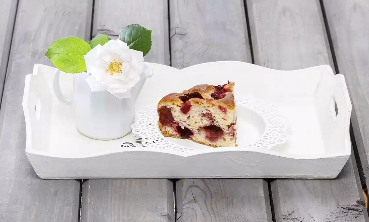 Felie de prăjitură pufoasă cu accente aurii și bucăți de căpșuni roșii suculente, așezată pe un șervet dantelat în tavă albă elegantă