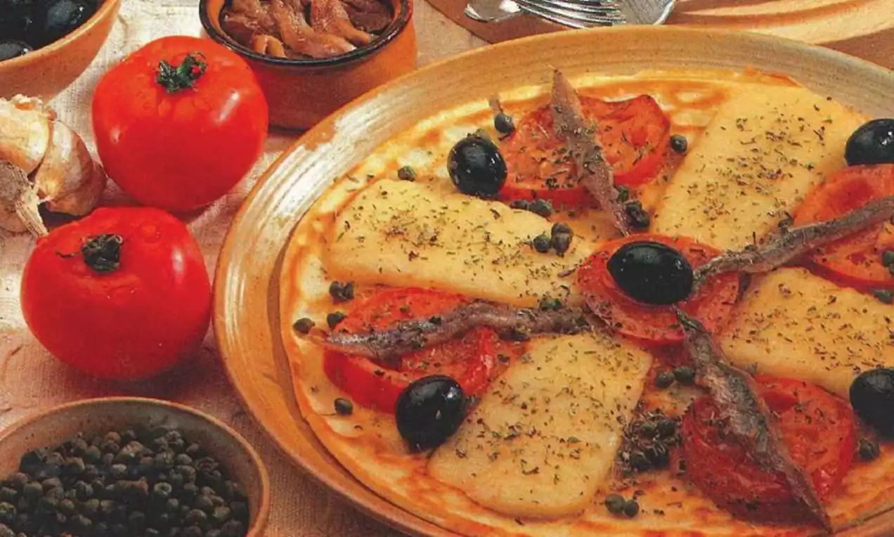 Dunne flensjes met goudbruine randen, belegd met tomaat, gesmolten kaas, zwarte olijven, ansjovis en kappertjes op een lichtbruin bord