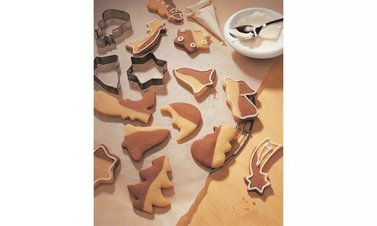 Çeşitli yılbaşı şekillerinde kesilmiş siyah-beyaz kurabiyeler, fırın kağıdı üzerinde metal kalıplar ve bir kase beyaz kremayla hazırlanmış
