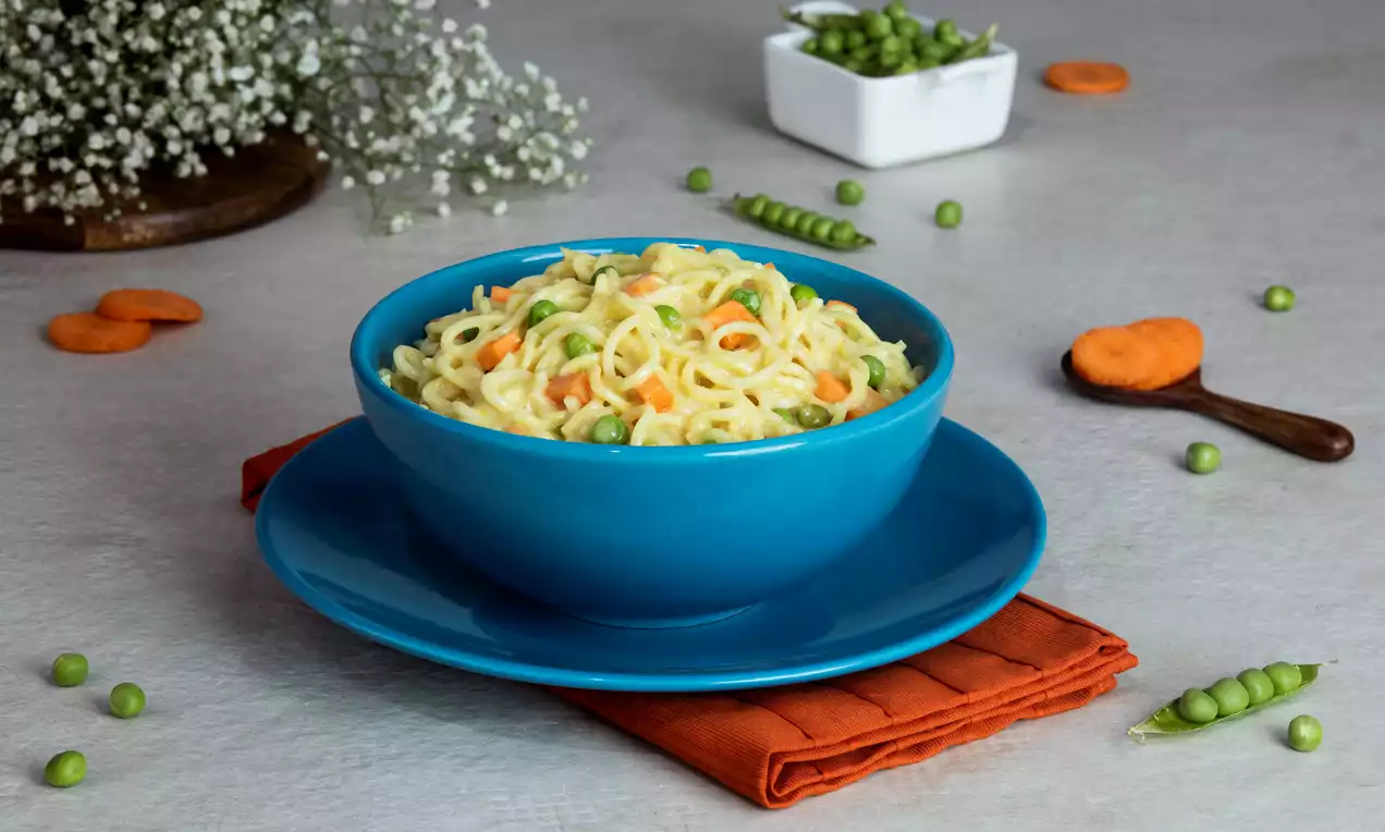 Creamy yellow noodles mixed with bright green peas and orange carrot pieces served in a smooth blue bowl on an orange napkin