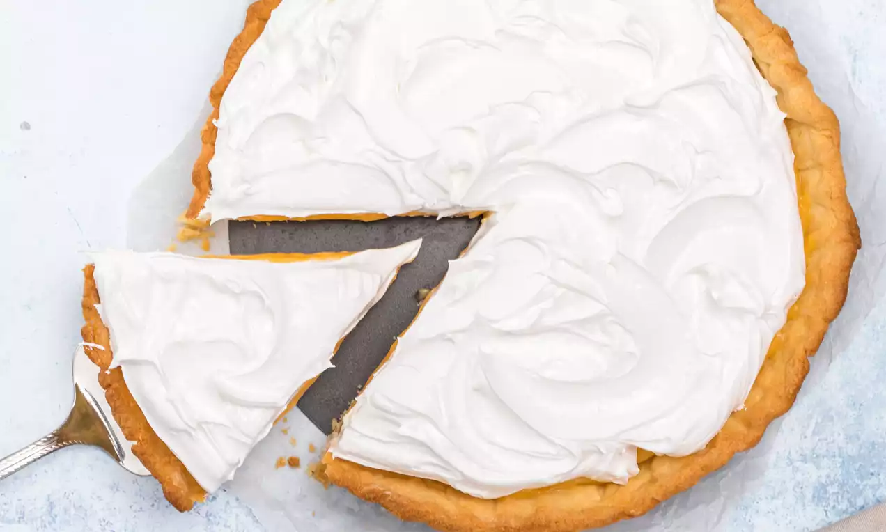 Pie de limón con masa dorada, relleno amarillo vibrante y capa ondulada de merengue blanco sobre papel y fondo claro