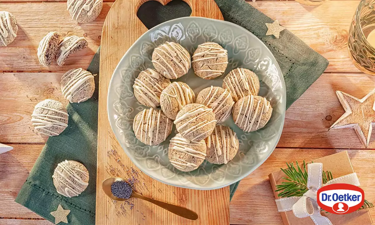 Kulaté makové cookies s jemnými bílými polevovými proužky, aranžované na ozdobném šedozeleném talíři, obklopené svátečními dekoracemi