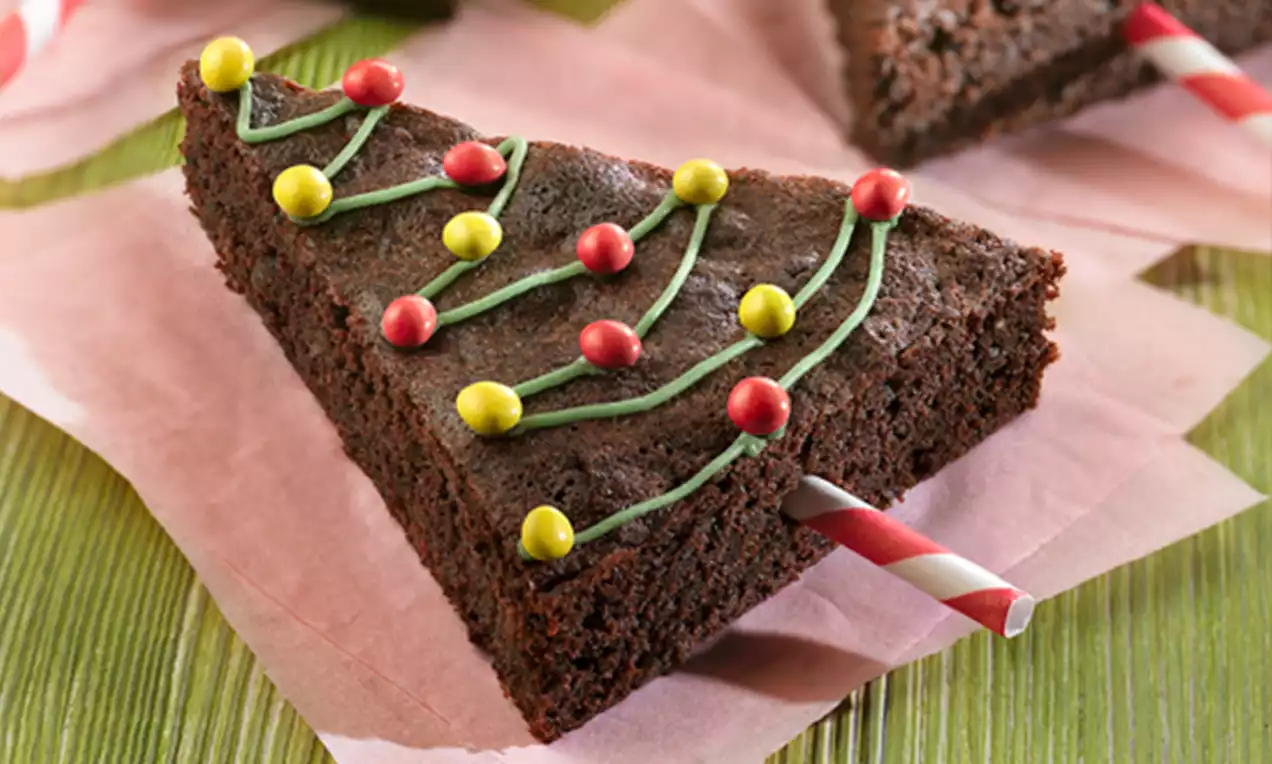 Triángulos de brownie oscuro con textura esponjosa decorados con líneas verdes y esferas rojas y amarillas sobre pajitas rayadas