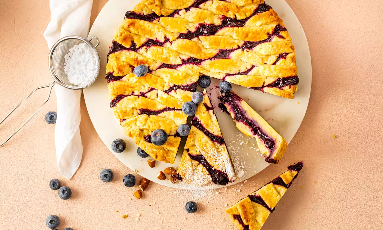 Gevlochten bosbessentaart met goudbruin raster van deeg, paarse bosbessenvulling en decoratie van verse bosbessen op een marmeren bord