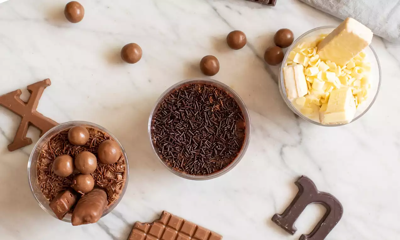 Tres bowls sobre mármol blanco, uno con bolitas y figuras de chocolate marrón, otro con virutas de chocolate oscuro y otro con chocolate blanco rallado
