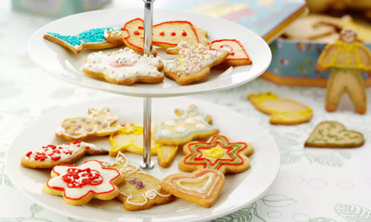 Småkaker med hvit og fargerik glasur i ulike former på et to-etasjers kakefat av hvit keramikk med metallhåndtak