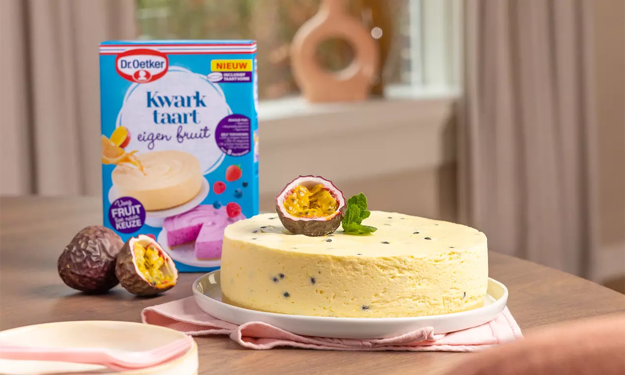 Passievrucht kwarktaart met gladde, pastelgele vulling vol donkere stipjes, gegarneerd met halve passievrucht en blaadje munt op een wit bord