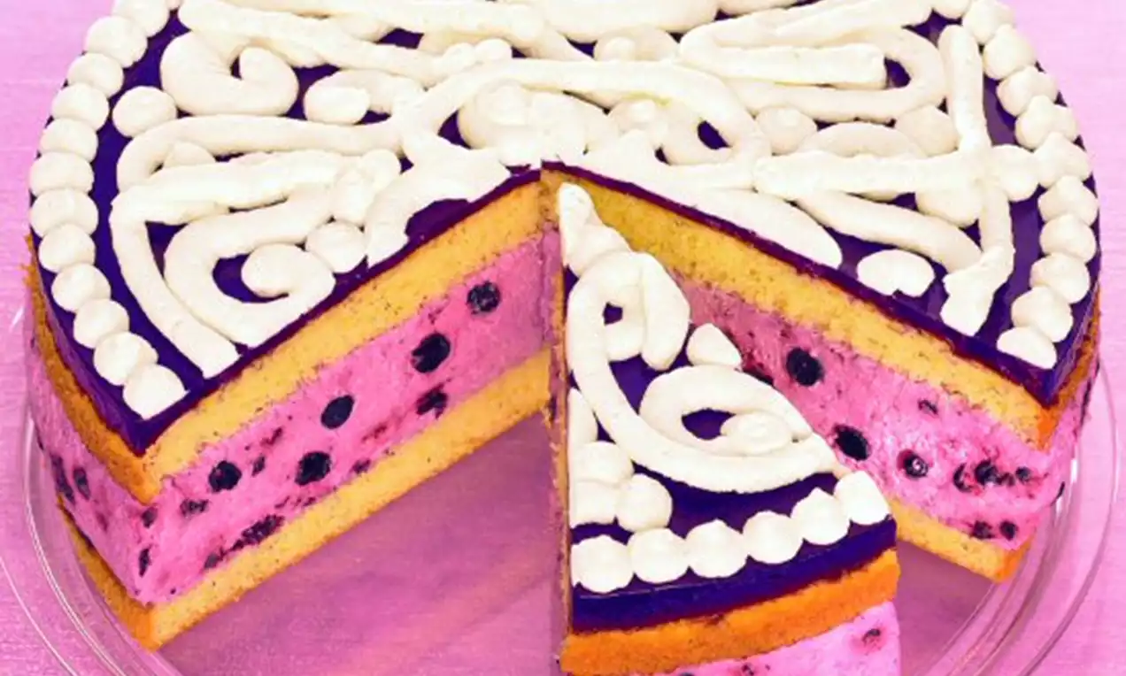 Zweischichtige Torte mit gelbem Biskuit, rosa Joghurtcreme und Heidelbeeren, weißer Sahnedekoration und lila Guss auf Glasplatte